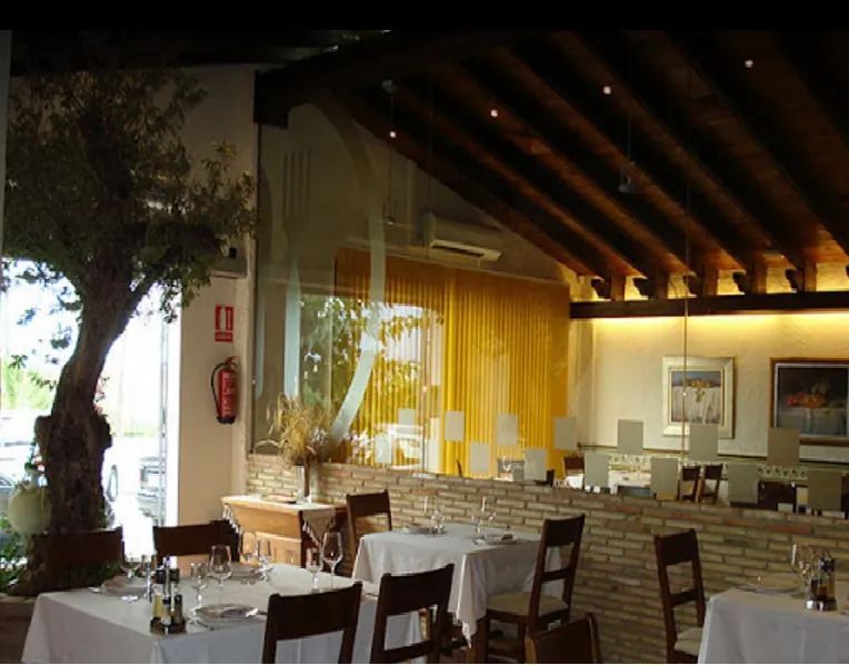 Comedor de La Masía con un olivo, vigas de madera y mesas vestidas